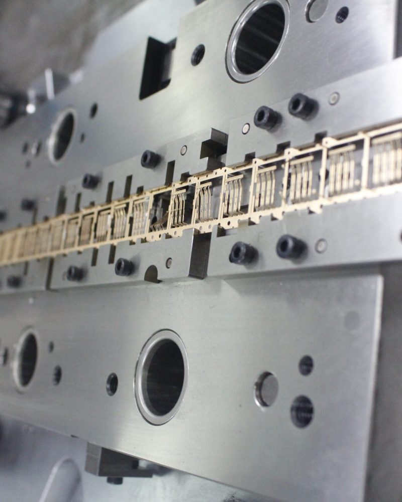 Custom multi-station stamping die with the part strip in its stations, built by SSP, a transfer stamping dies manufacturer in China